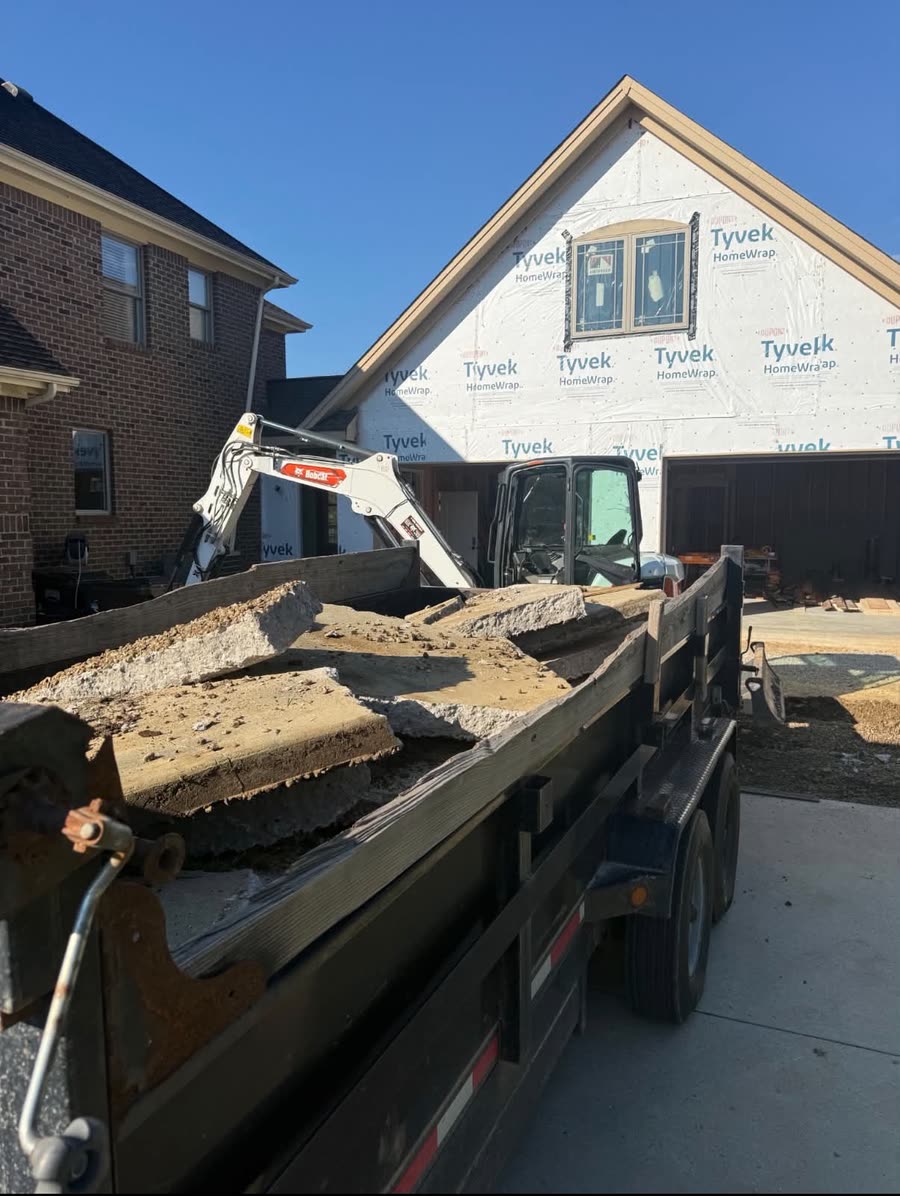 Broken concrete slabs loaded into a dump trailer beside a mini excavator