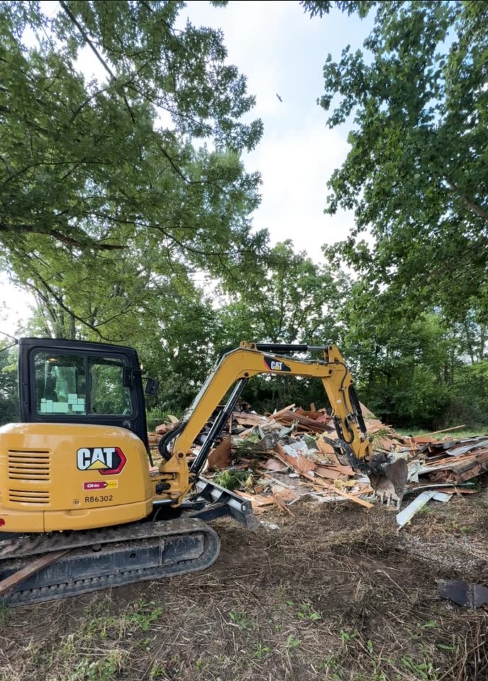 A CAT excavator tearing out a structure with the debris piled beside it