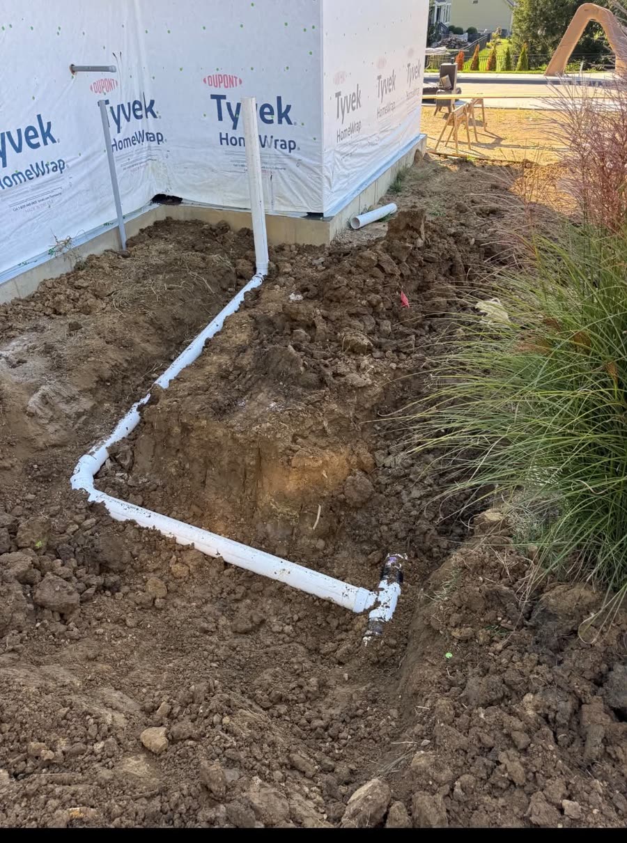 White PVC downspout drain lines routed underground around a house foundation