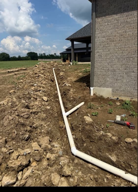 A new white PVC drain line run along the foundation of a brick house