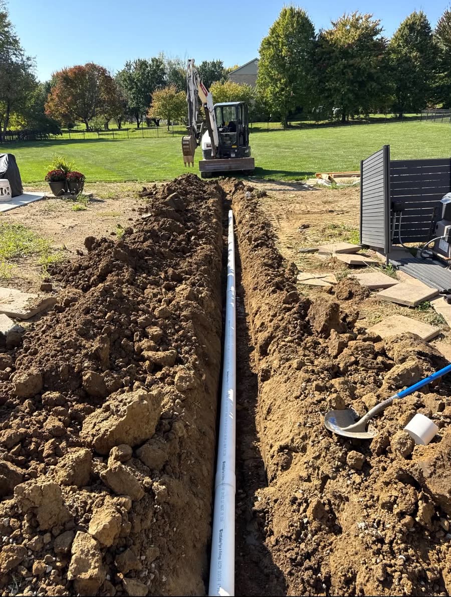 A trench with new drain pipe laid, excavator standing by