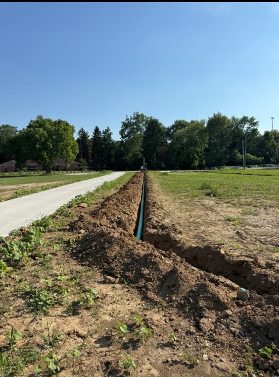 A long drain line laid in an open trench beside a concrete drive