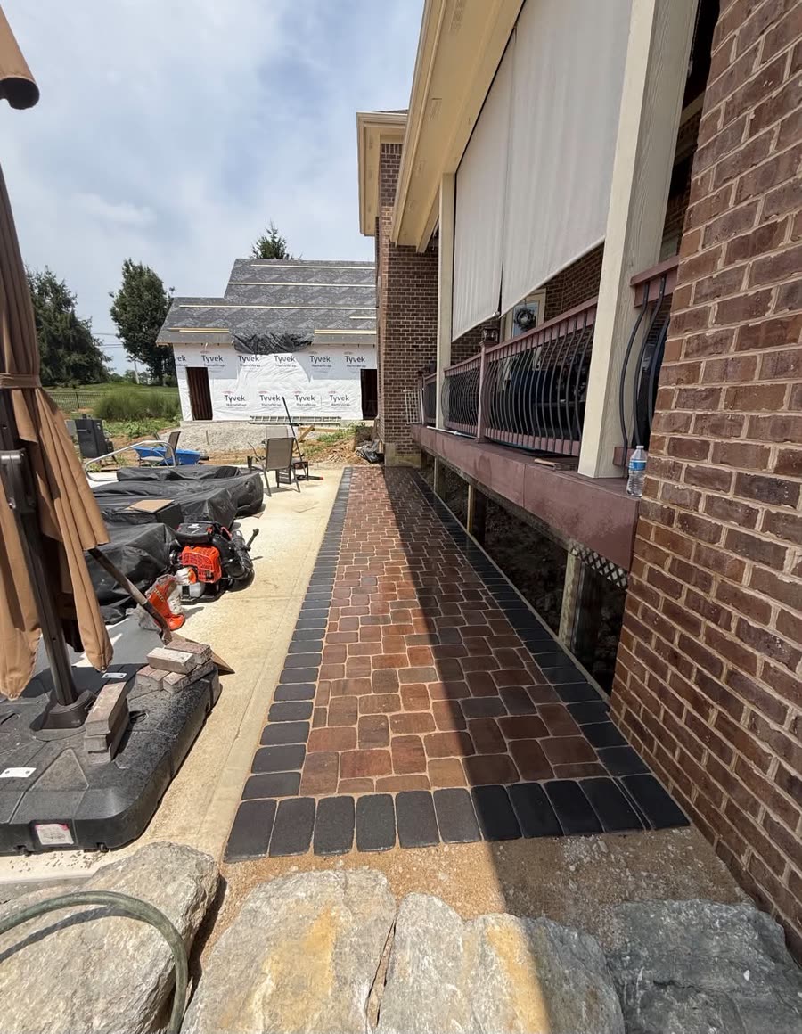 A paver walkway in red and charcoal along a brick house